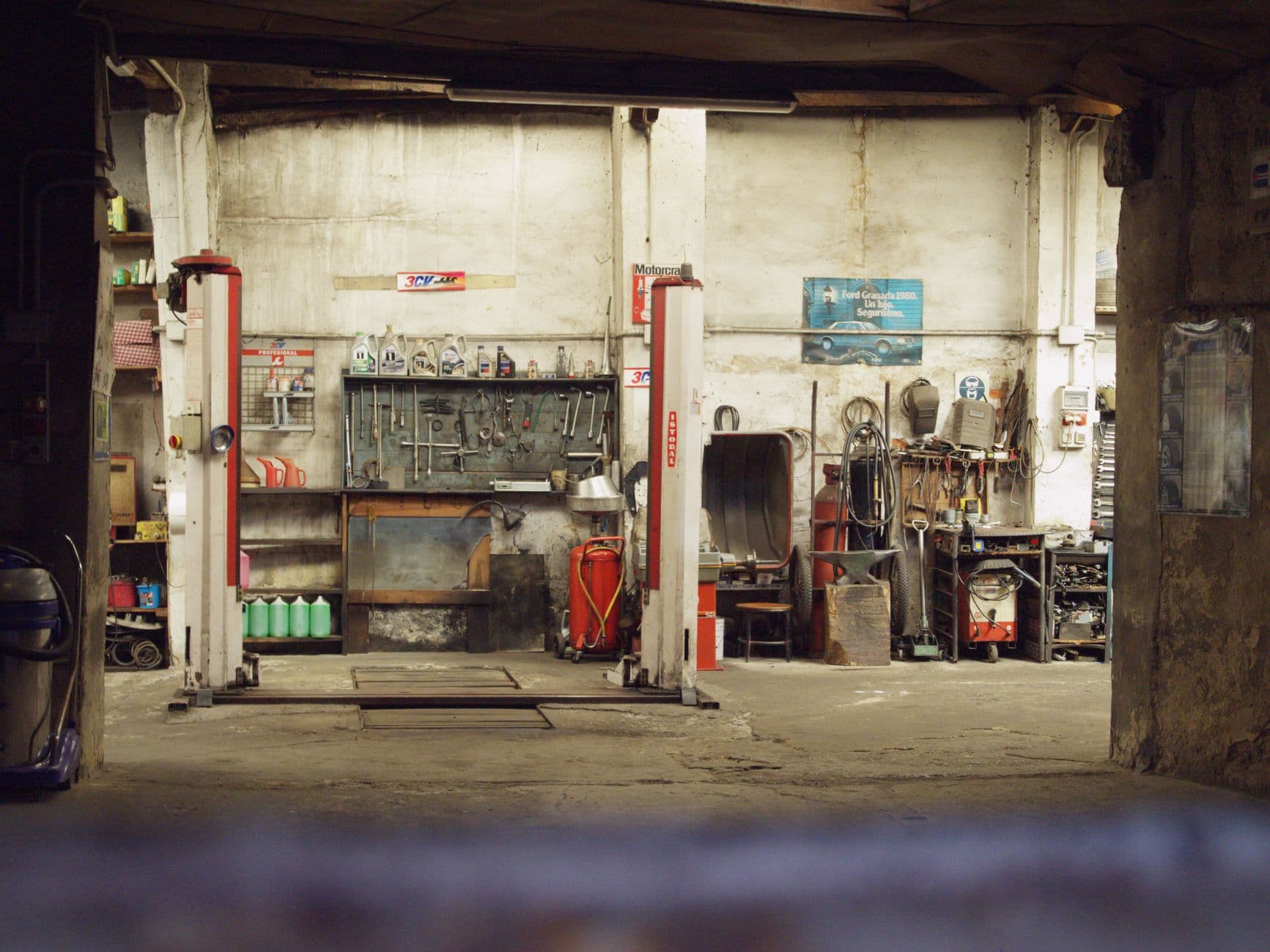 An empty, rustic car workshop featuring tools, machinery, and car lifts in an industrial setting.